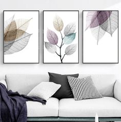 three leaf paintings on the wall above a white couch in a room with black and white pillows