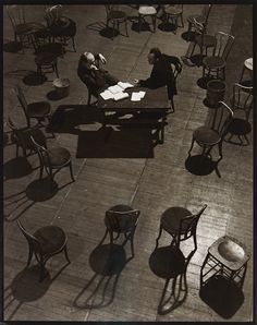 black and white photograph of people sitting at desks in an open area with chairs