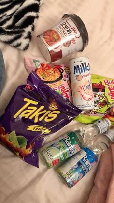 a person is laying on a bed with snacks and drinks in their hands, along with other food items