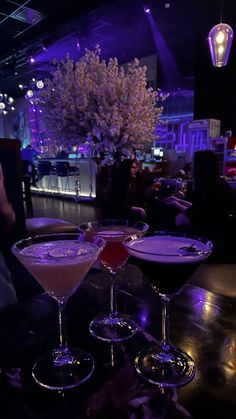 three martinis sitting on top of a table in front of a purple lit bar