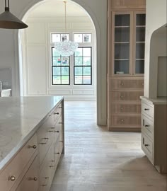 an arched doorway leads to a large kitchen with marble counter tops and white cabinets, along with a chandelier hanging from the ceiling