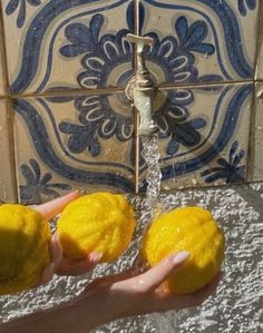 two lemons are being held under a faucet with water running from it