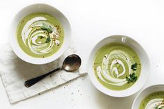 two white bowls filled with green soup on top of a table next to a spoon