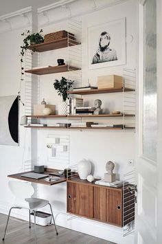 a white room with shelves filled with books and vases next to a desk, chair