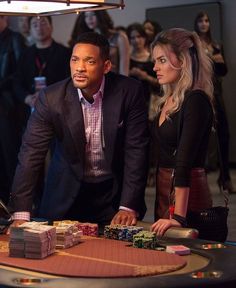 a man and woman playing cards at a casino table with other people in the background