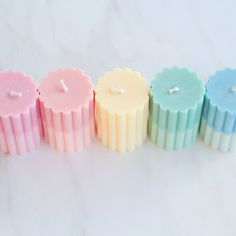 five different colored candles lined up on a white counter top with one candle in the middle