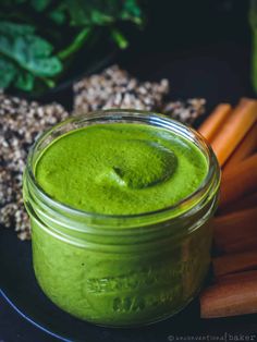 a glass jar filled with green liquid next to carrots