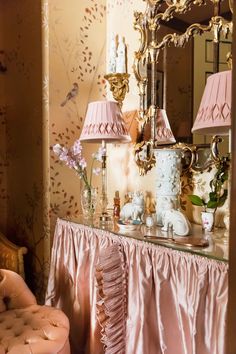 there is a pink chair in front of a mirror and table with two lamps on it