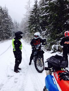 three people standing in the snow next to a motorcycle and sled on a snowy road