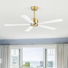 a living room with a ceiling fan and large window overlooking the ocean in front of it