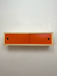 an orange shelf mounted to the side of a white wall with two black dots on it