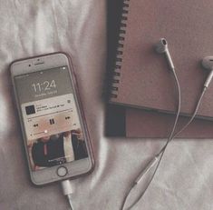 an iphone and headphones are laying on a bed next to a notebook with ear buds