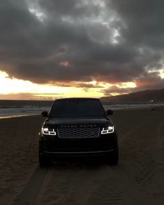 a black range rover parked on the beach at sunset with dark clouds in the background