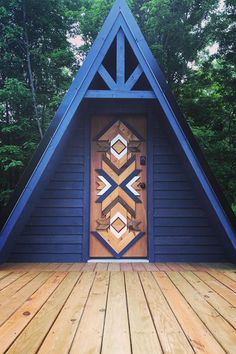 a wooden deck with a triangle shaped door in front of it and trees behind it