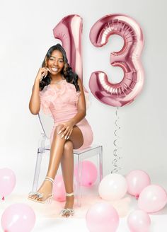 a woman sitting on a chair in front of pink balloons and streamers with the number thirteen