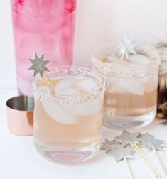 two glasses filled with pink liquid next to a copper shaker and star shaped straws