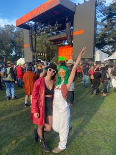 two women standing in front of a stage at an outdoor music festival with their arms up