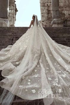 a woman in a wedding dress is standing on some stairs with her veil flowing over her head