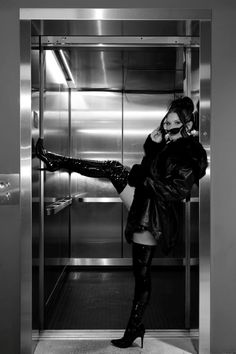 a woman standing in an elevator talking on the phone and holding onto her thigh high boots