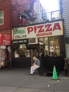 a man sitting in front of a pizza shop