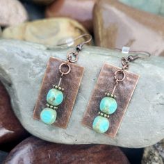 the earrings are made with copper and turquoise beads on top of brown leather, sitting on some rocks