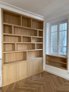 an empty room with wood flooring and open bookshelves on the wall next to a window