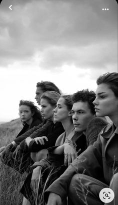 a group of people sitting on top of a grass covered field next to each other