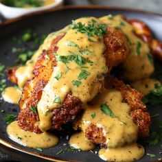 some meat covered in gravy and garnished with parsley on a black plate