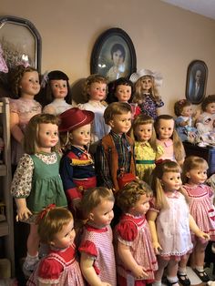 a group of dolls standing next to each other in front of a wall with pictures on it