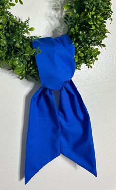 a blue scarf hanging on the wall next to some green leaves and plants in front of a white wall