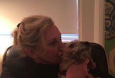 a woman is kissing her dog on the cheek while sitting in a chair next to a window