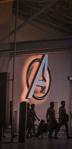 several people walking past a sign with the avengers logo on it