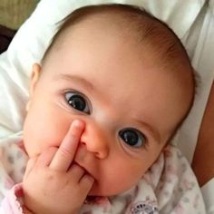 a close up of a baby laying on top of a bed holding its hand to her face