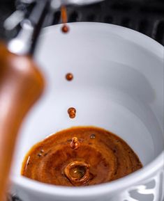 an espresso being poured into a white coffee cup with caramel colored liquid