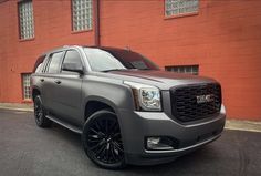 a grey suv parked in front of a red building with black rims on it