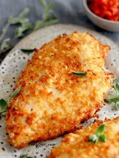 two pieces of fried chicken on a plate next to a small bowl of tomato sauce