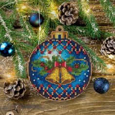 a cross stitch ornament hanging from a christmas tree with pine cones and ornaments