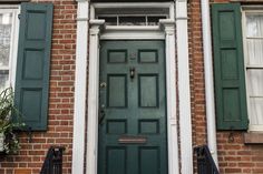 a green door with two windows and shutters on the side of a brick building