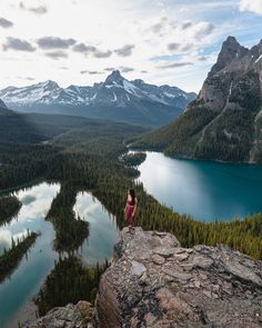 a woman sitting on top of a rock next to a lake and mountains in the background