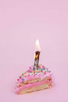 a piece of cake with pink frosting and sprinkles on it is lit by a single candle