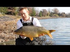 a man holding a large fish while sitting on a rock next to a body of water