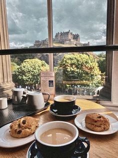 two cups of coffee and cookies on a table in front of a window overlooking the city