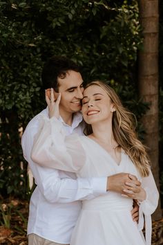 a man and woman hugging each other in front of some trees with their eyes closed