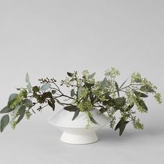 a white vase filled with green plants on top of a table