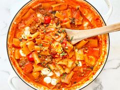 a pot filled with pasta and meat in tomato sauce on top of a marble counter