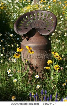 an old rusty watering can sitting in the middle of a field full of wildflowers