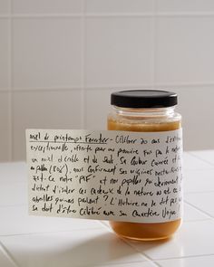 a jar filled with honey sitting on top of a white tiled counter next to a piece of paper