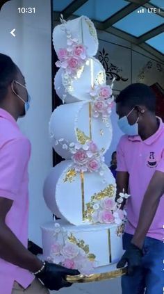 two people in pink shirts are standing near a large cake