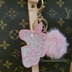 a pink and silver keychain with a butterfly on it's side, attached to a louis vuitton bag