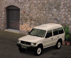 a white suv parked in front of a stone building with potted plants next to it